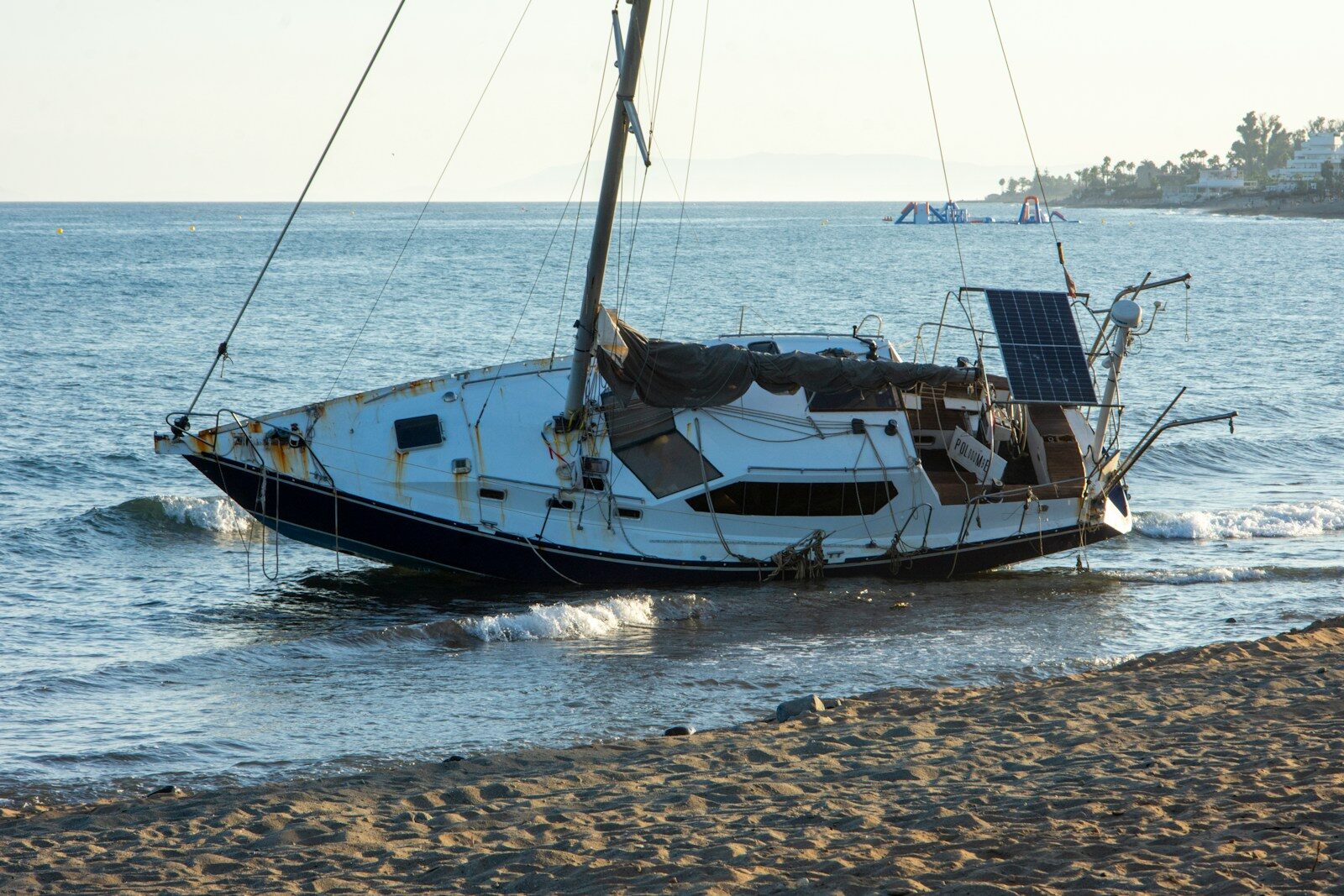 Weathered sailboat stranded on a sandy beach near the ocean.